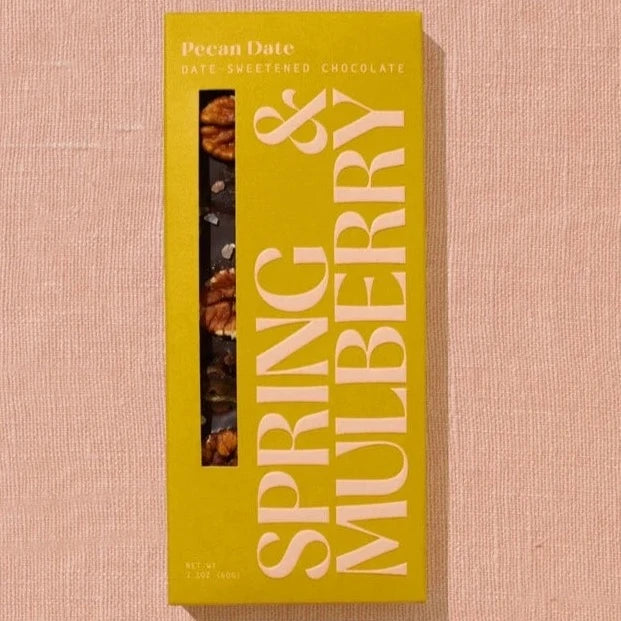 A rectangular chocolate bar packaged in mustard yellow paper with beige text reading, "Pecan Date"