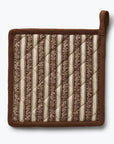 A square quilted pot holder with a brown suede-like border and handle, featuring vertical striped patterns in cream and brown on the front, shown against a light gray background.
