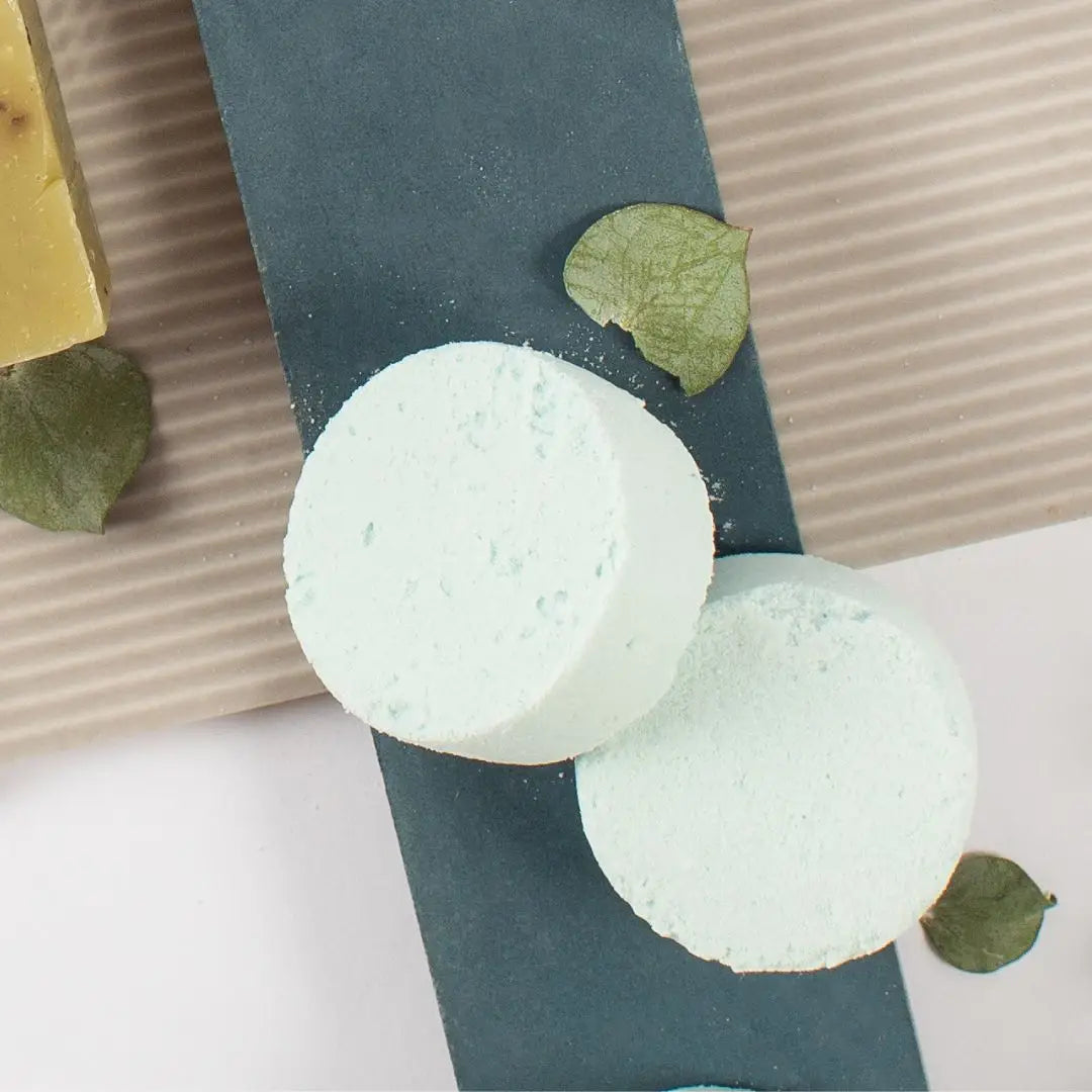 Two green bath bombs on a textured surface with leaves around