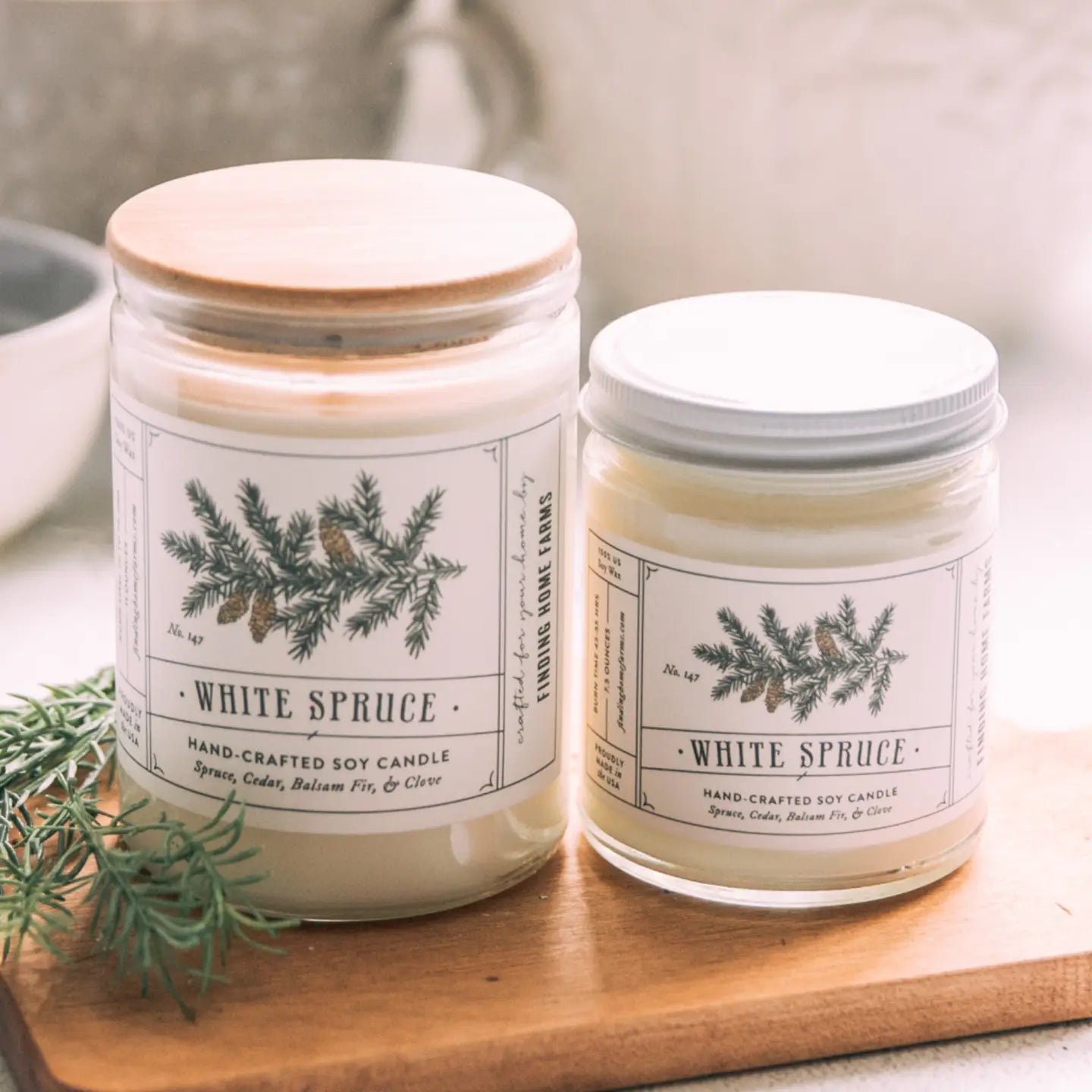 Two White Spruce candles on a wooden board with a neutral background