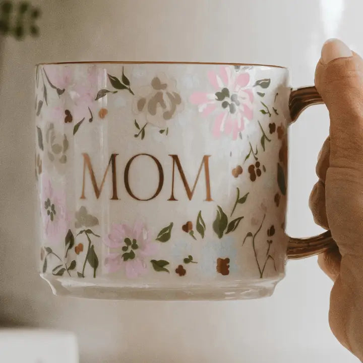 Mug with floral design and 'Mom' text held by a hand