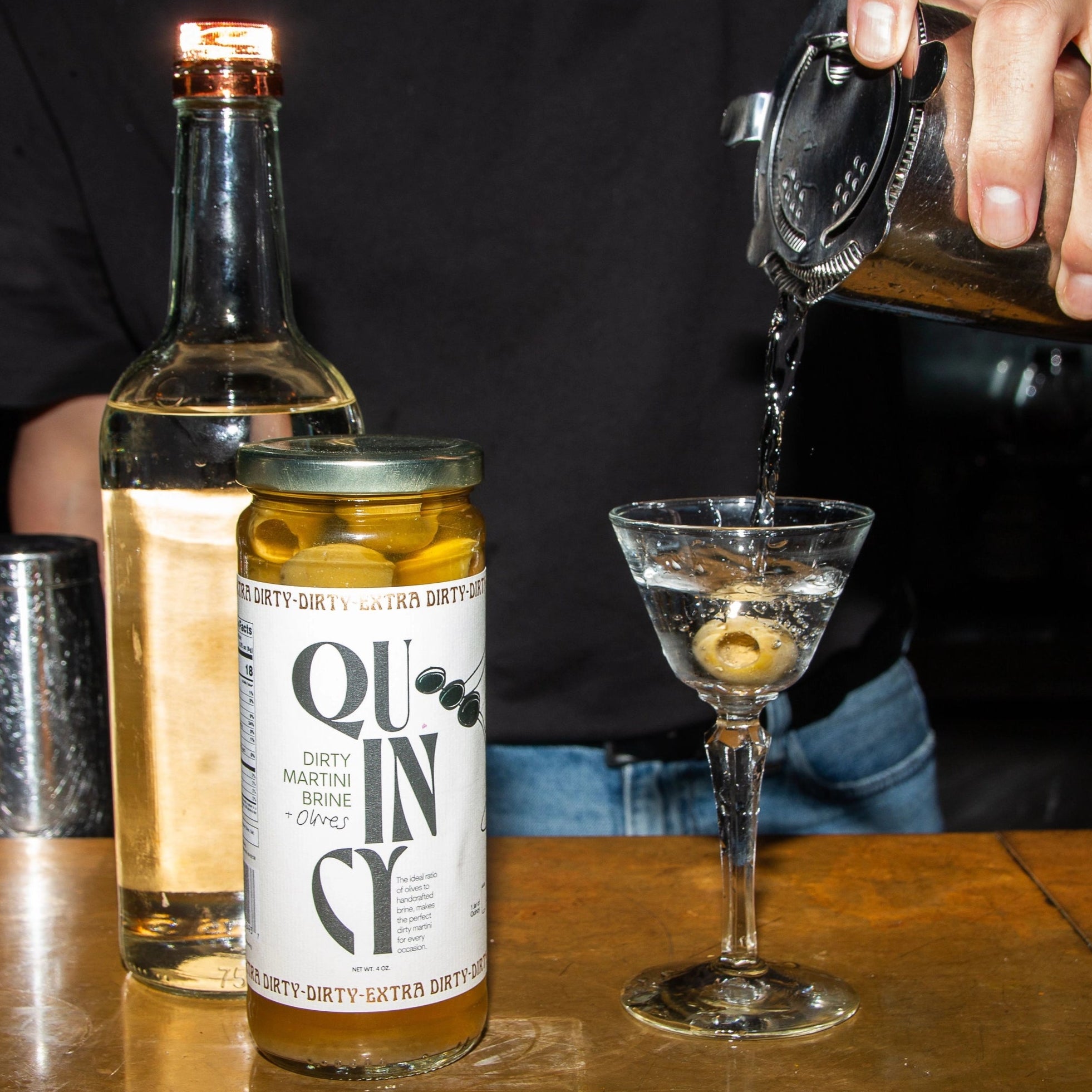 Bar setting with a bottle of gin, a cocktail glass, and a person pouring a drink.