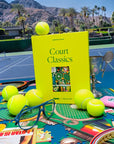 Book titled 'Court Classics' on a tennis court with tennis balls and other items.
