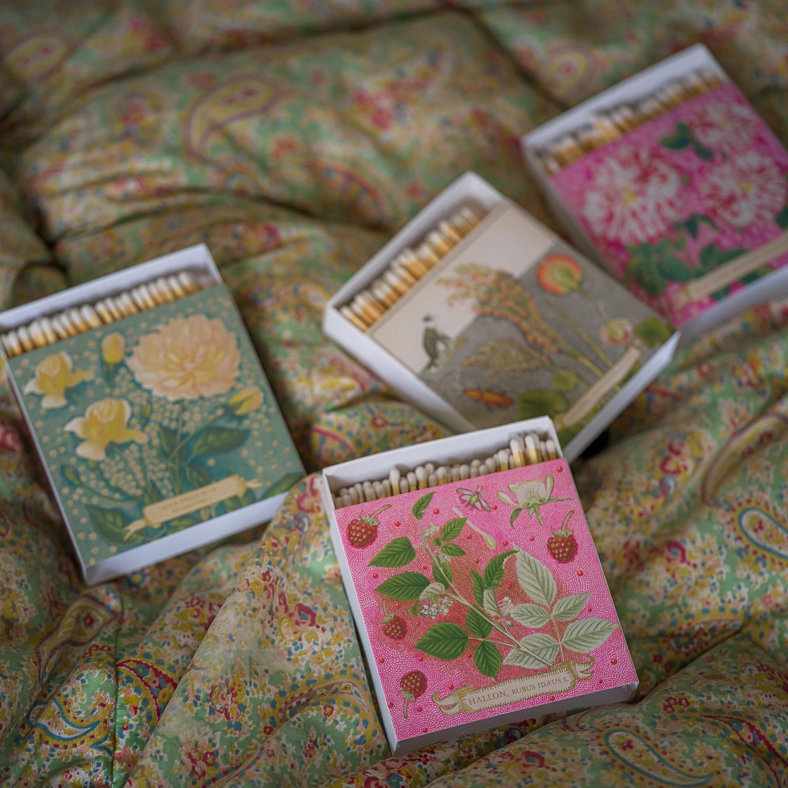 Matchboxes with floral designs on a patterned fabric background