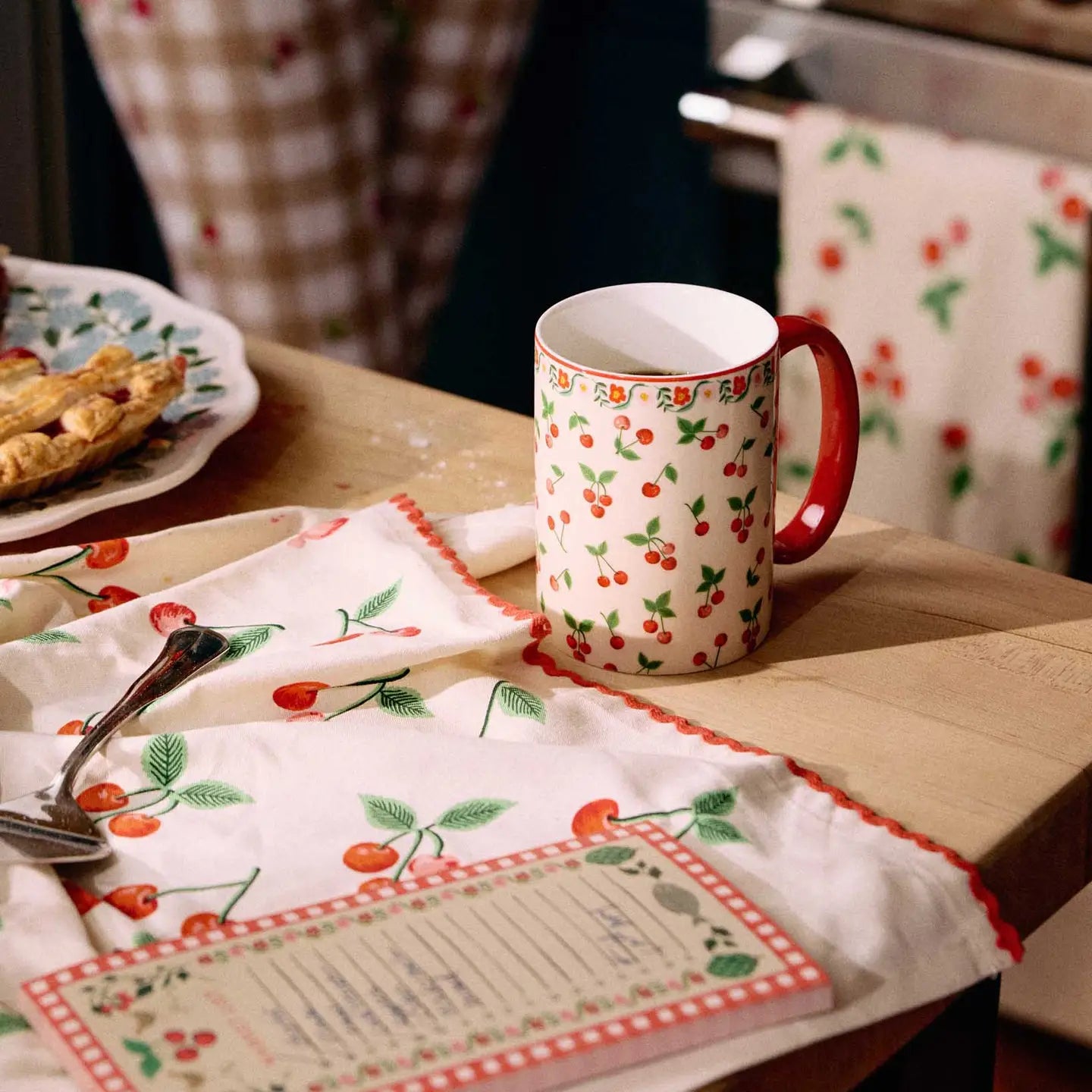 cherry porcelain mug on a table with a cherry cloth spoon and notepad