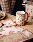 cherry porcelain mug on a table with a cherry cloth spoon and notepad