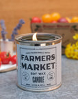 Farmers Market soy wax candle in a metal canister with a wooden background and fruits.