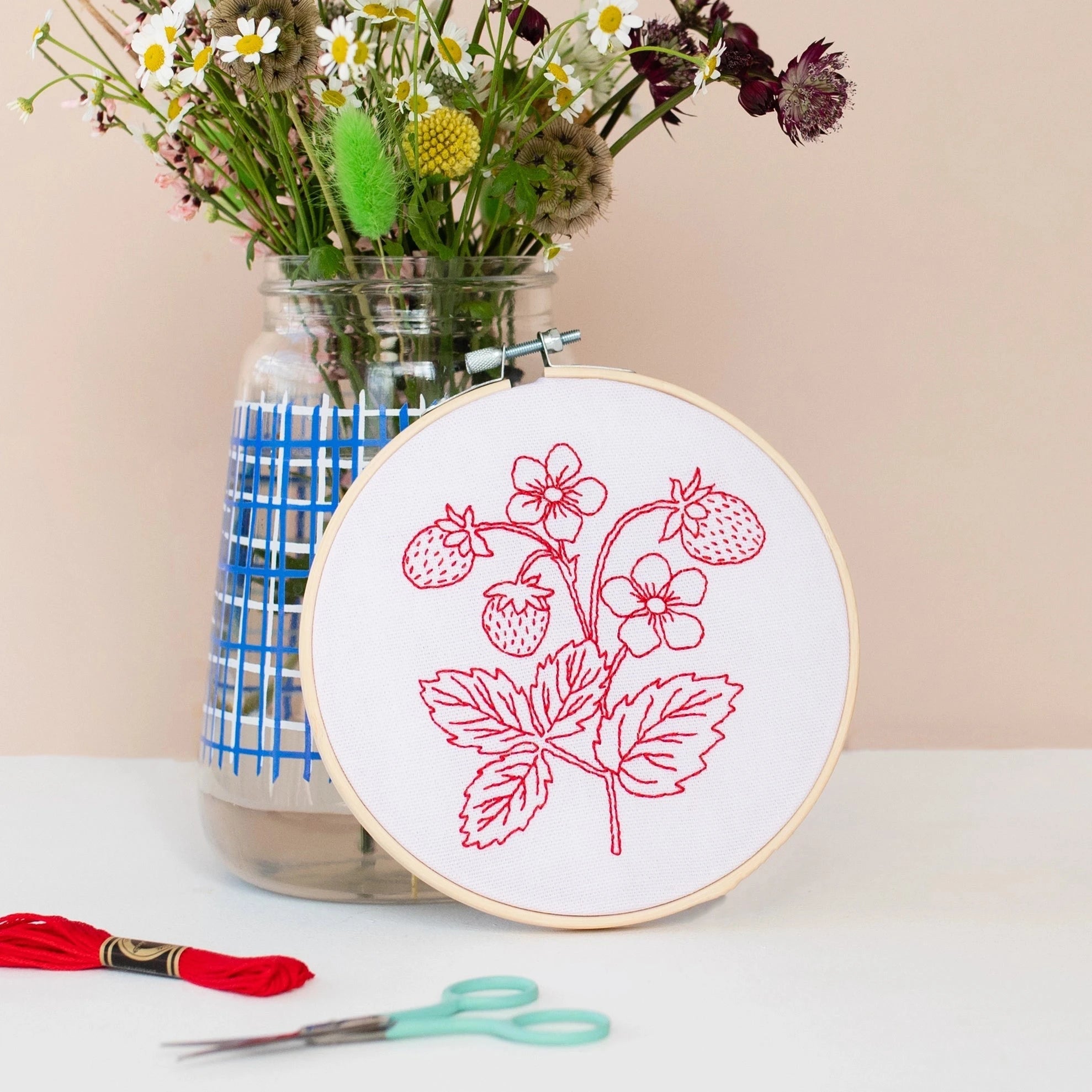 strawberry embroidery hoop leaning on a vase