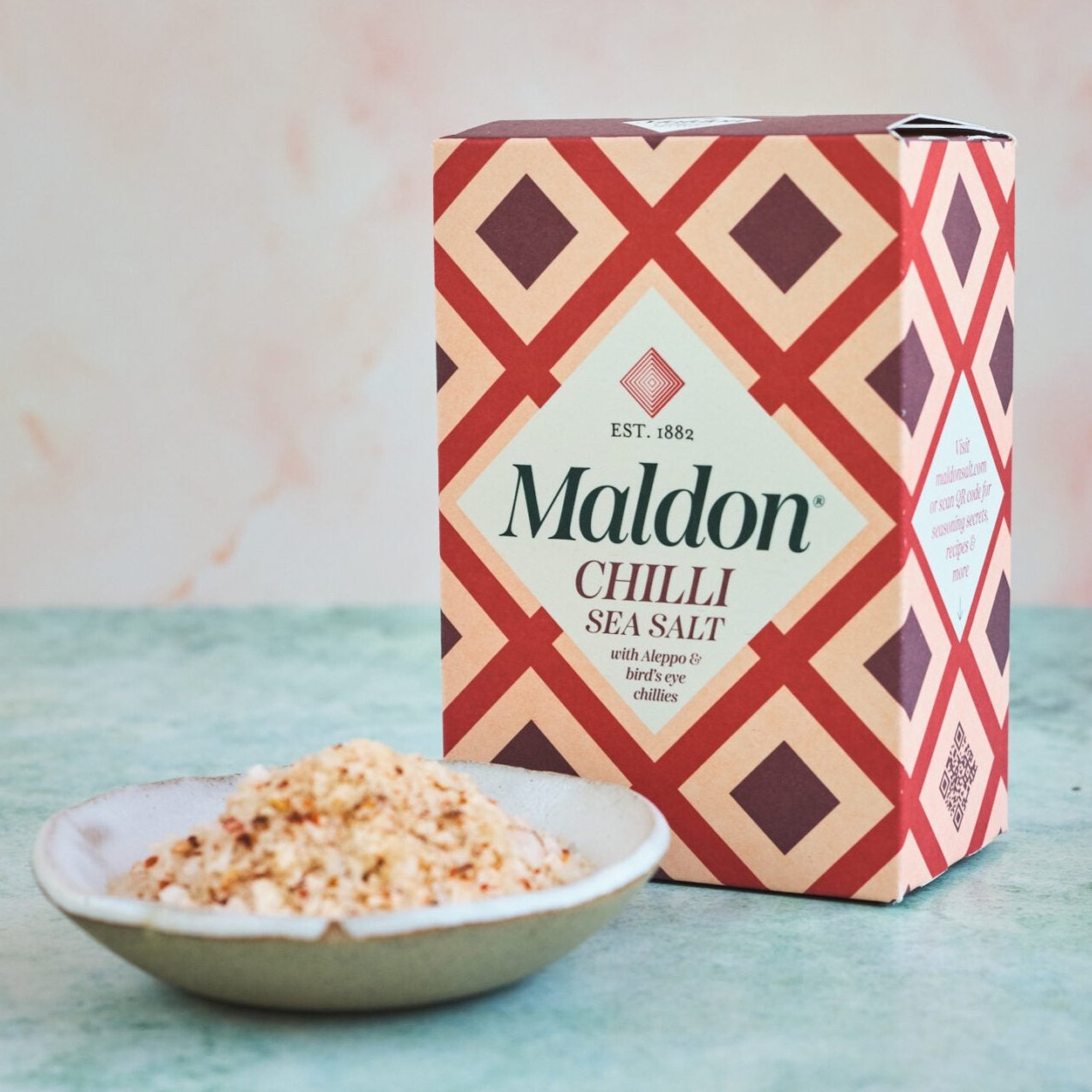 box of Maldon Chilli Sea Salt placed behind a bowl of the salt itself.