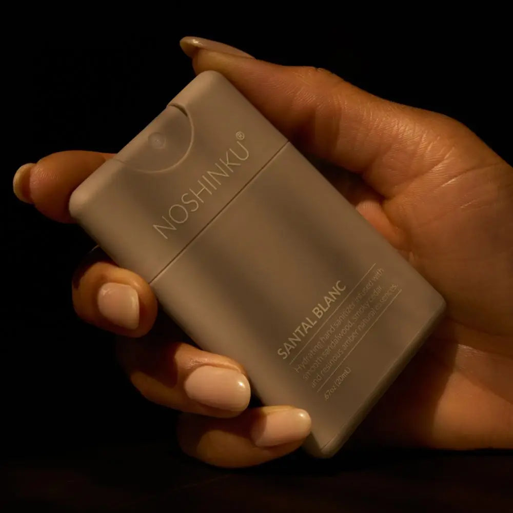 Hand holding a Noshinku Santal Blanc perfume bottle against a dark background