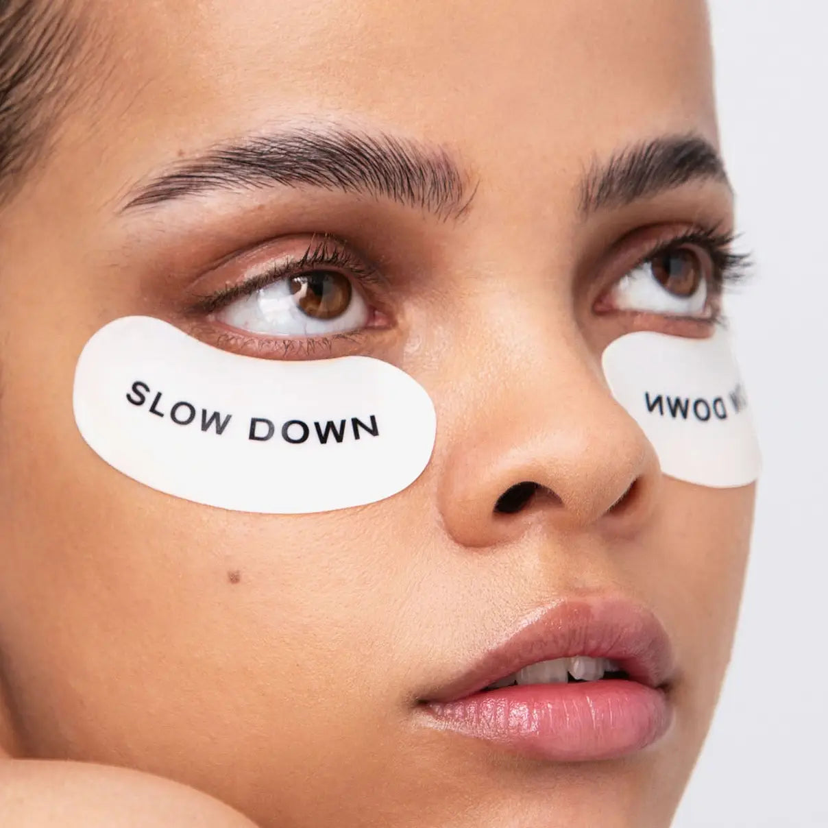 Close-up of a person's face with eye patches labeled 'SLOW DOWN' on a plain background