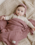 Baby wrapped in a pink blanket with a matching headband, lying on a textured surface.