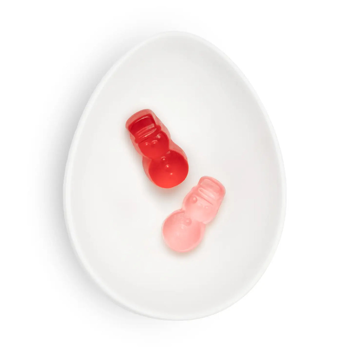 Two small gummy candies shaped like snowmen, one translucent red and one translucent pink, displayed on a white oval dish against a white background.