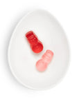 Two small gummy candies shaped like snowmen, one translucent red and one translucent pink, displayed on a white oval dish against a white background.