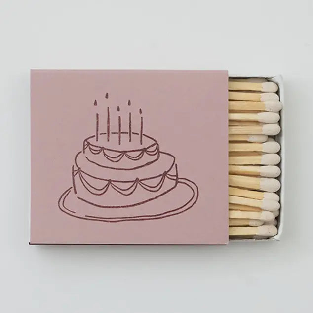 Matchbox with a pink cover featuring an illustration of a cake with candles on a white background