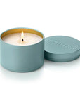 A teal blue metal candle tin with a lit wick and cream-colored wax, shown next to its matching lid which features the brand name 'APOTHEKE' embossed on a clean white background.