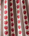 A close-up of a fabric pattern featuring vertical stripes with red apples, brown gingham, and a central brown-and-white checkered stripe on an off-white background.