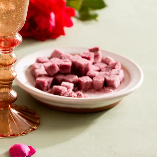 Pink cubes on a white plate with a decorative glass and red flowers in the background