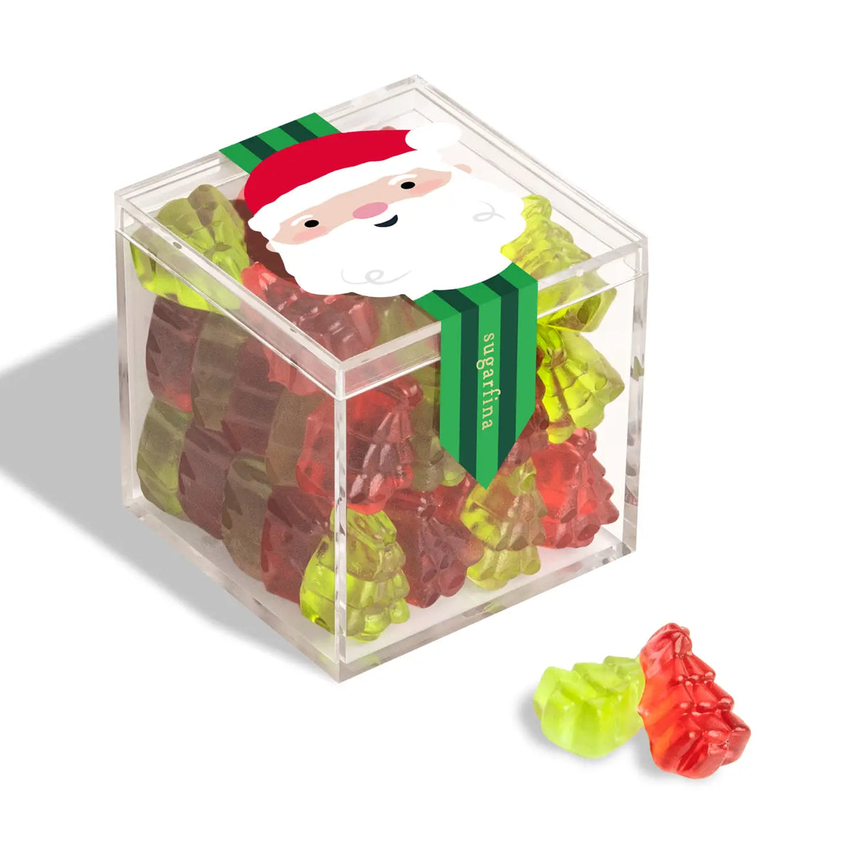A clear acrylic cube container filled with colorful gummy bears, tied with a green ribbon featuring a Santa face. Two loose gummy bears sit in front on a white background.