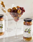 Two jars of olives with a martini glass filled with olives on a light background