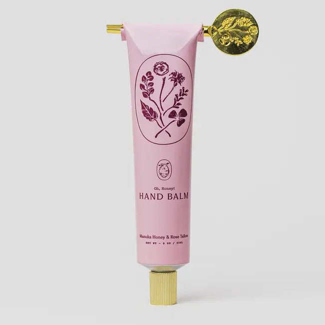 Pink hand balm tube with floral design and gold cap on a white background