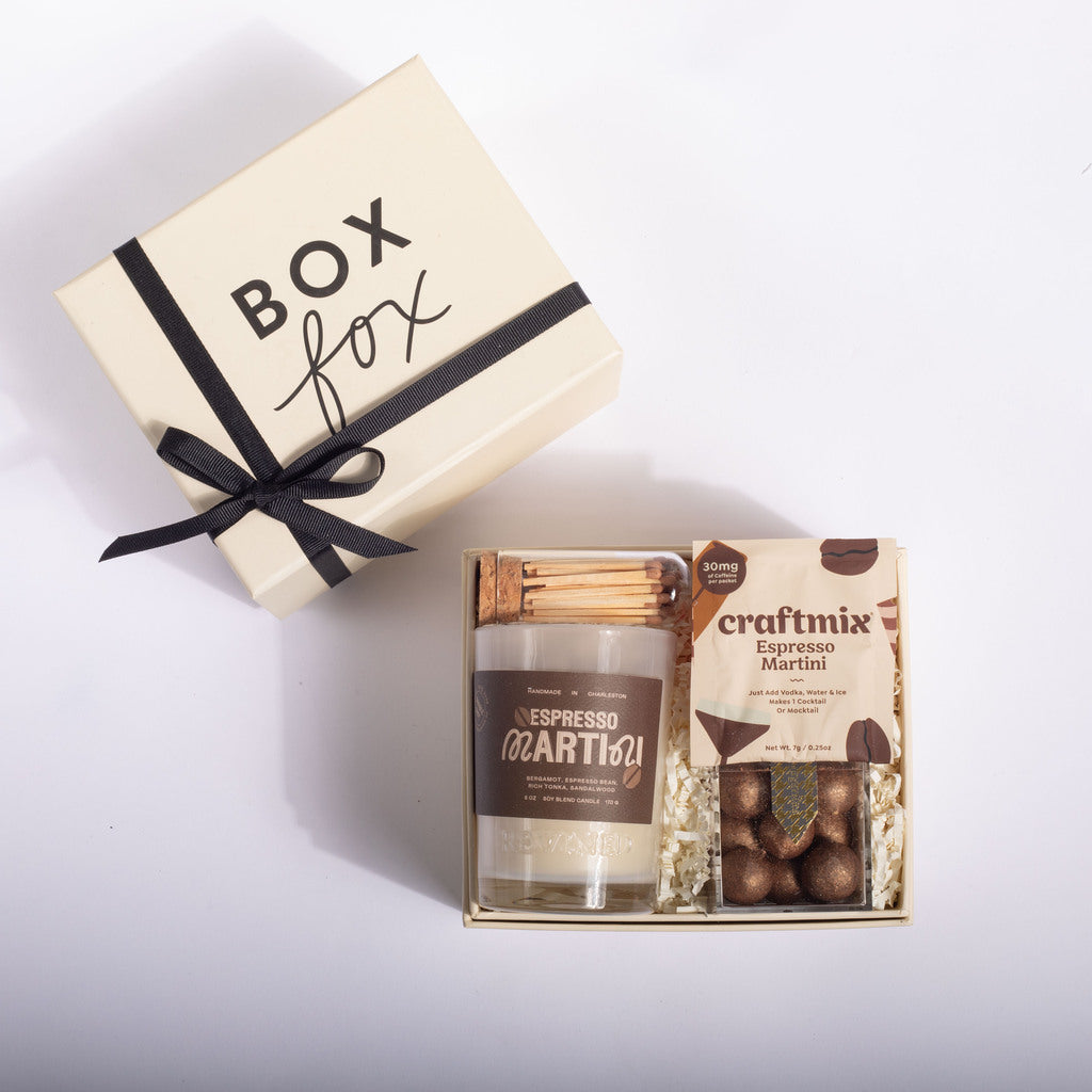A gift box set on a white background, featuring a cream-colored 'BOX fox' box with a black ribbon, next to an open gift tray containing a candle labeled 'ESPRESSO COFFEE' and a bag of 'craftmix Espresso Martini' chocolates.