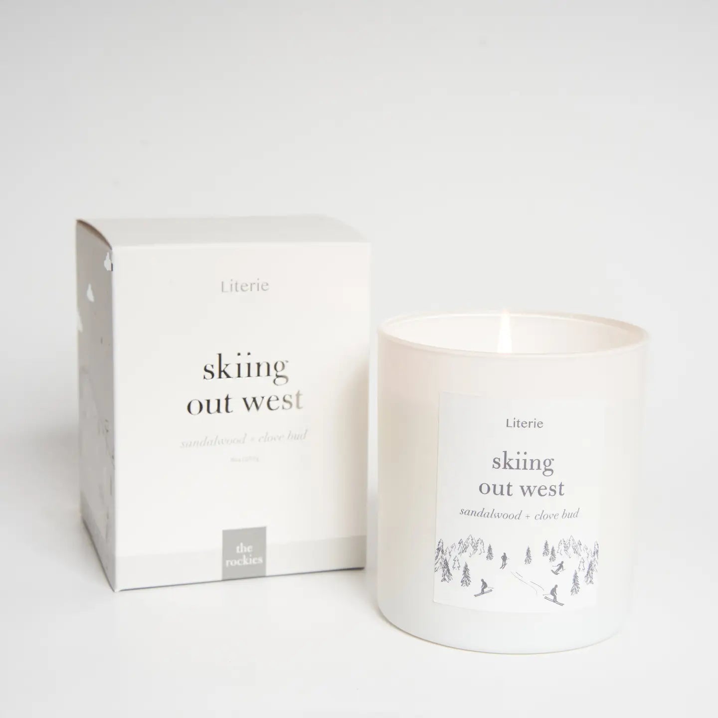 Candle and packaging with 'skiing out west' text on a white background