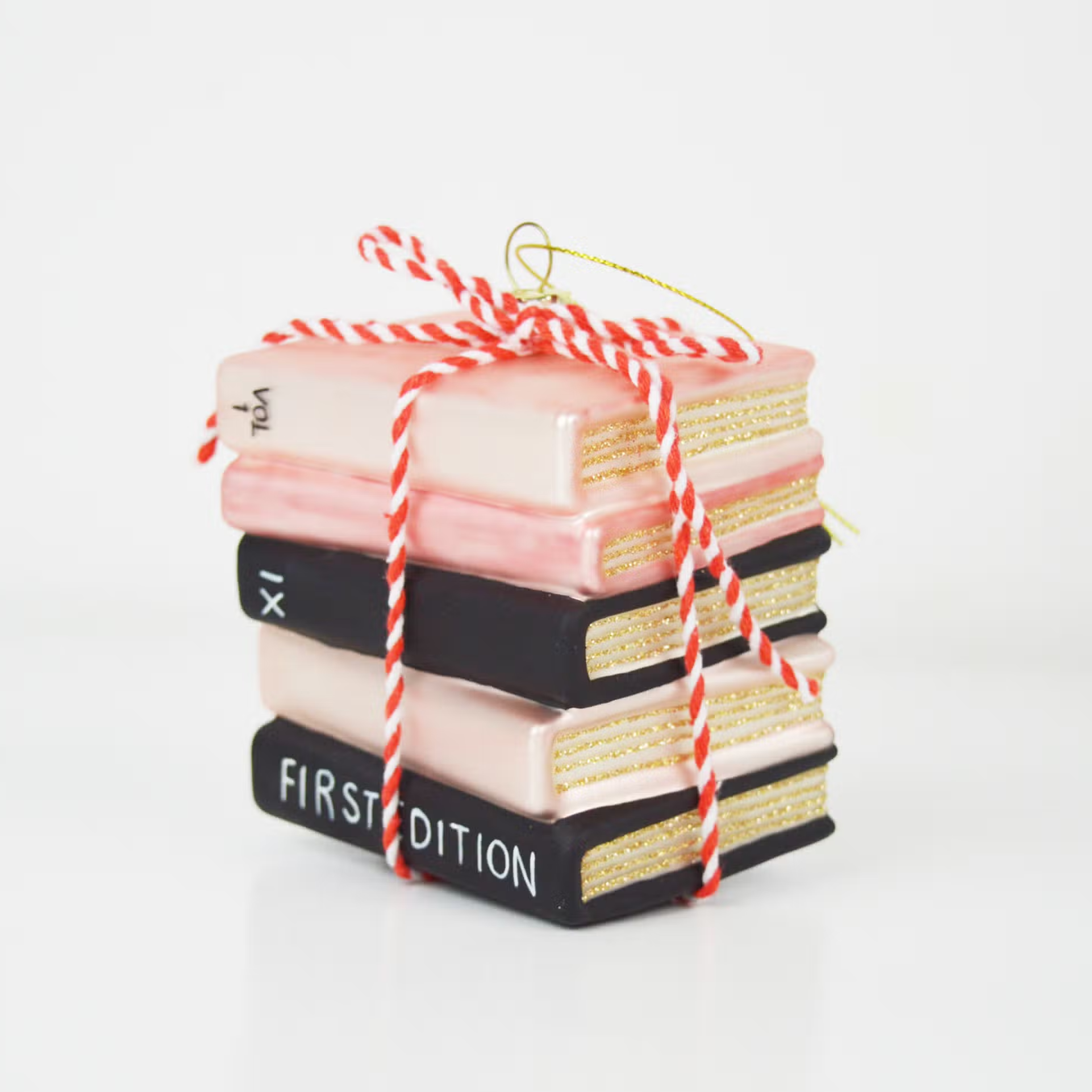 ornament shaped like a stack of book tied together with red and white twine. Book are pink and black with gold glitter showing the pages. 