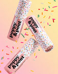 Three 'Poppy & Pout' lip balm tubes with colorful sprinkles on a gradient background