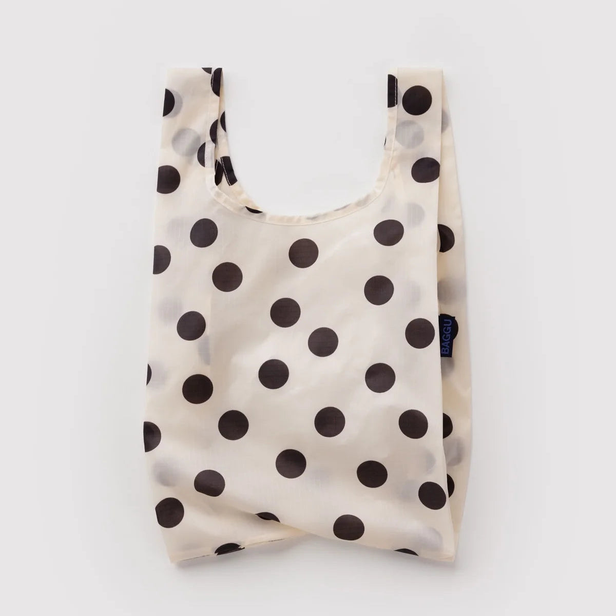 A reusable fabric shopping bag with a black polka dot pattern on a cream background, shown against a light gray studio backdrop.