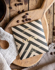 Coffee package with striped design on a wooden board with coffee beans and a cup of coffee.