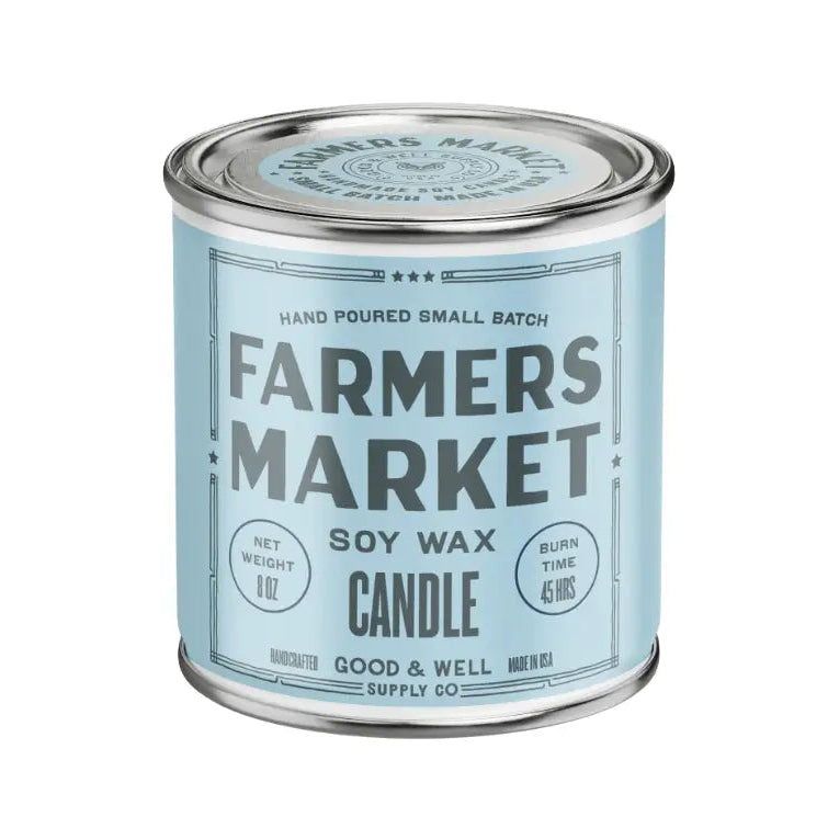A cylindrical metal tin candle with a light blue label reading 'FARMERS MARKET' and 'SOY WAX CANDLE' on a plain white background.