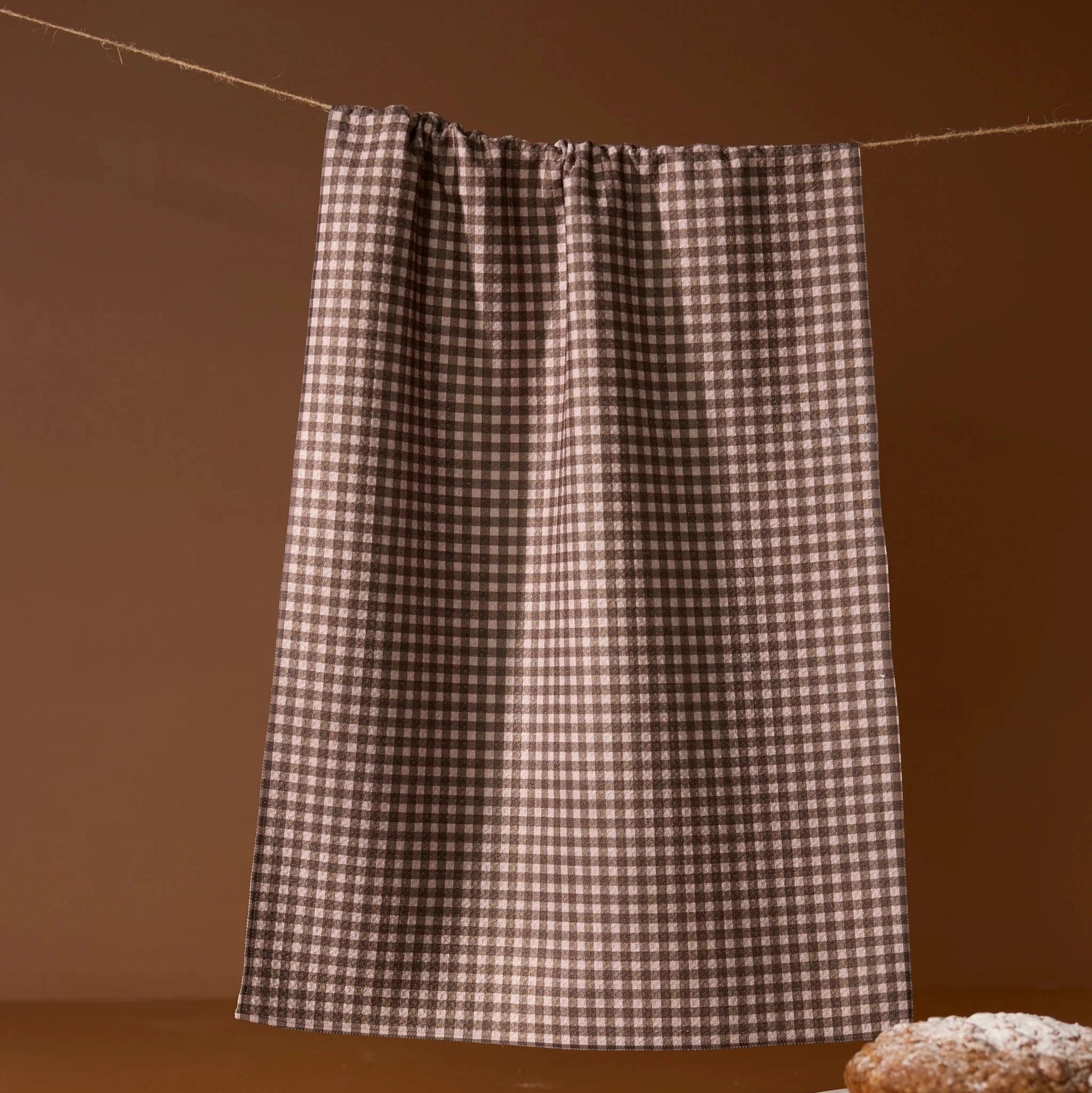 Checkered towel hanging on a line with a brown background and a pastry on a plate.
