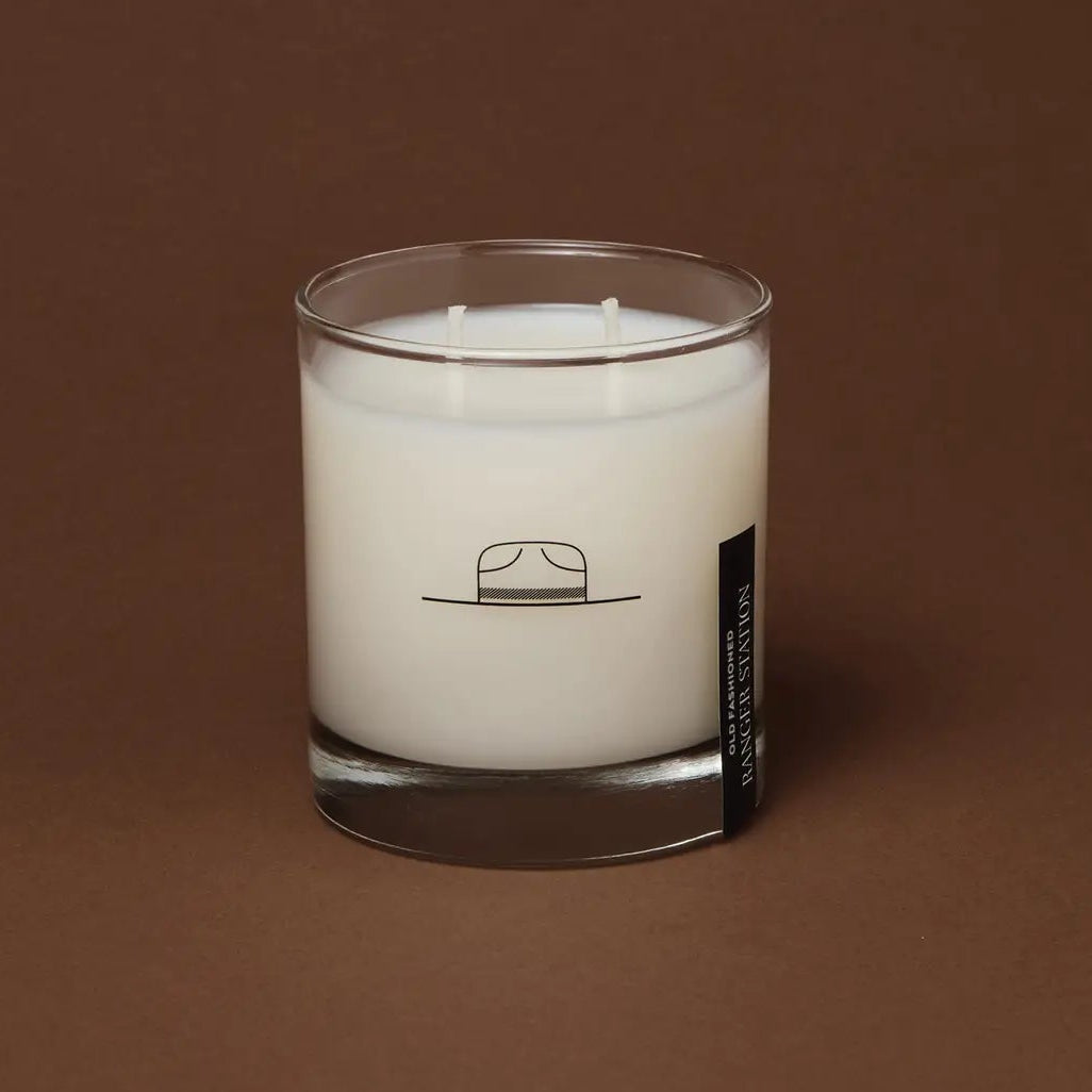 White candle in a glass jar with a label on a brown background