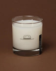 White candle in a glass jar with a label on a brown background
