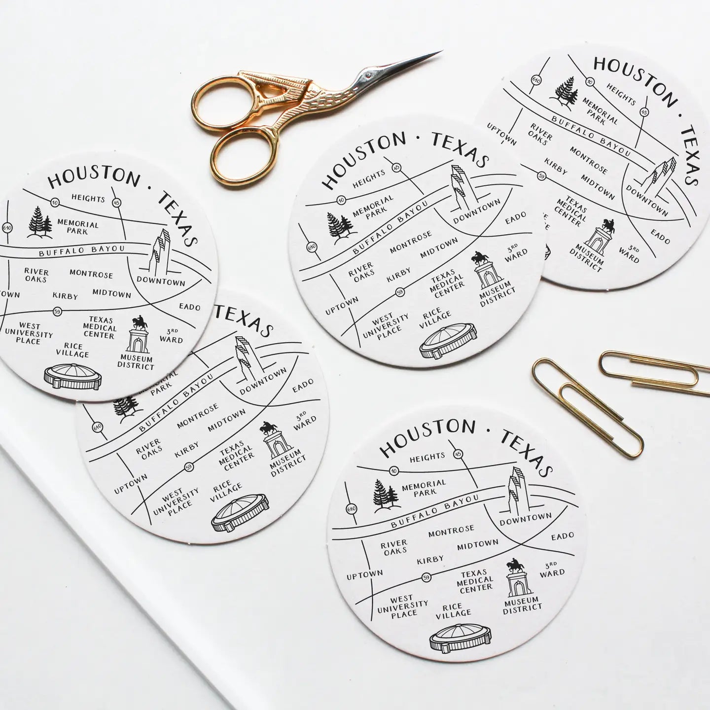 Houston, Texas-themed coasters with cut-out designs on a white surface with scissors and paper clips.