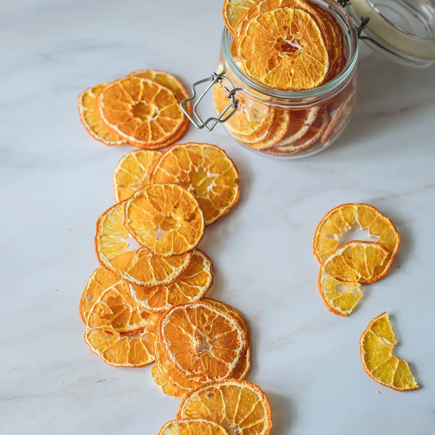 Dried orange slices on a marble surface with a jar of more dried oranges.