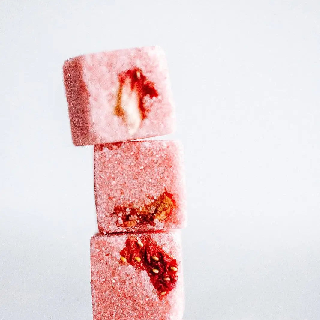 Three pink sugar cubes with red strawberry pieces on a white background