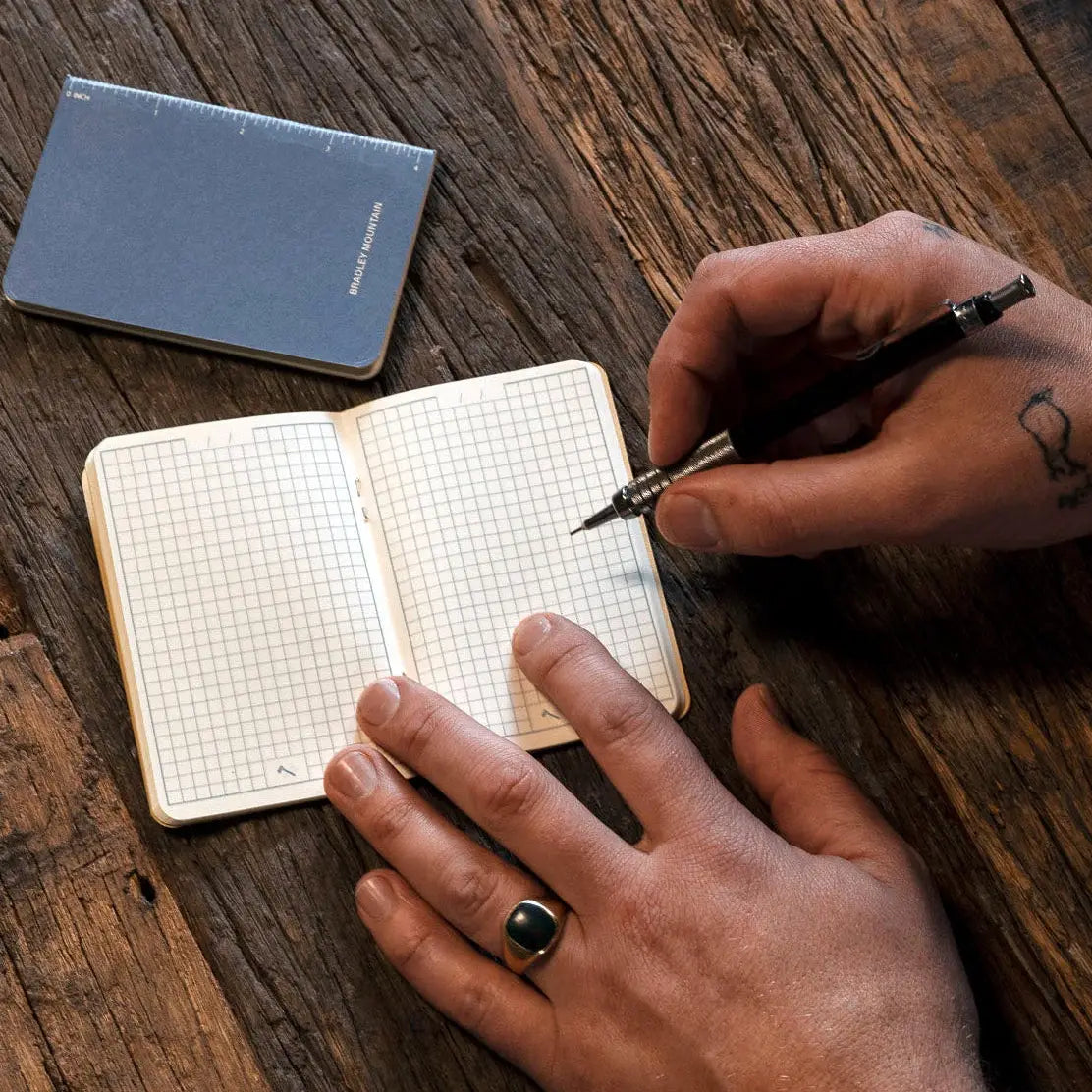 Person writing in a small notebook with a pen on a wooden surface