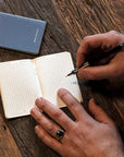 Person writing in a small notebook with a pen on a wooden surface