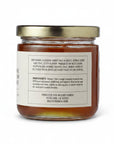 A glass jar of Mevyo Ranch Orange Blossom Honey with a gold metal lid and a white label showing the back text, set against a plain white background.