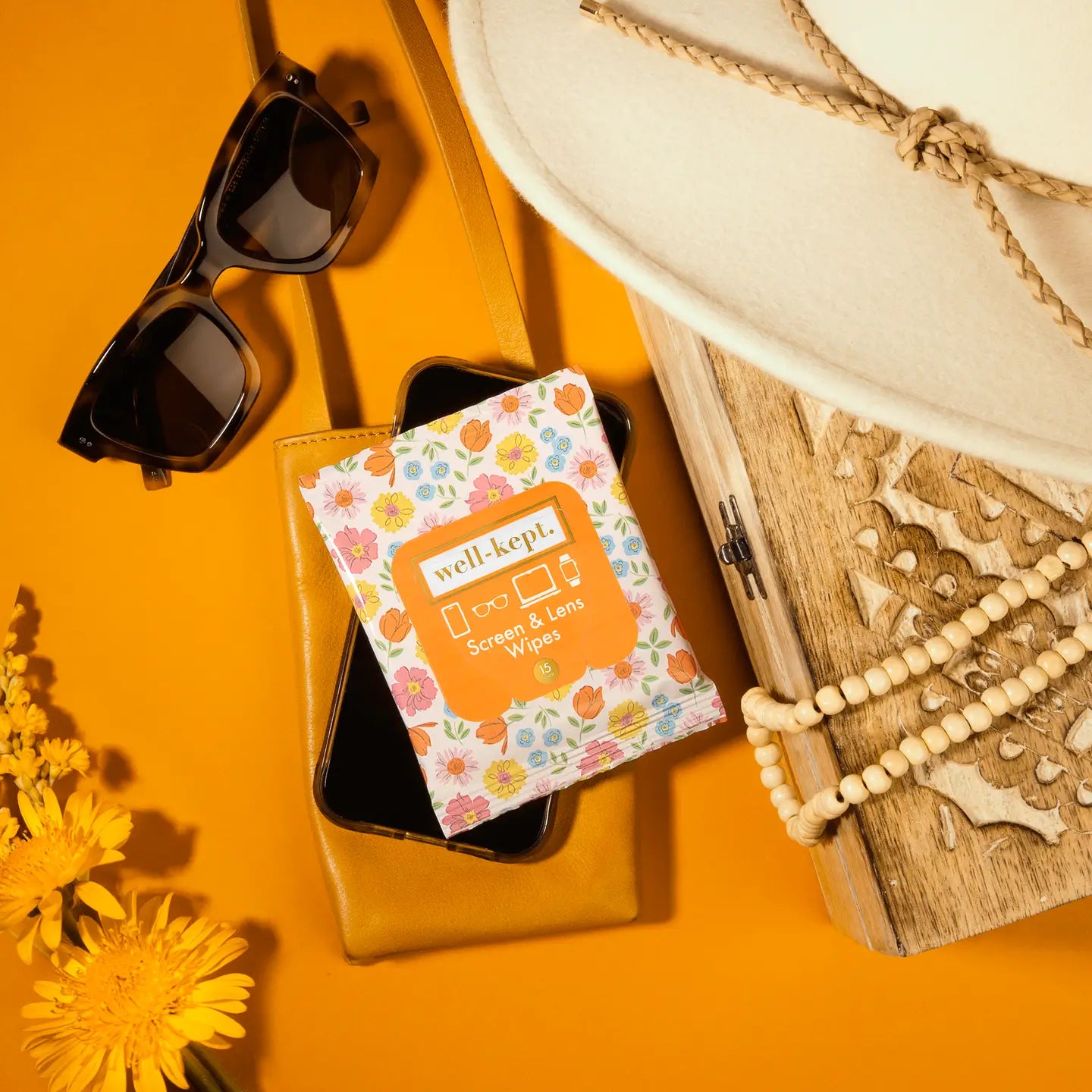 Phone case with floral design and 'well.kept' branding on an orange background with sunglasses, hat, and book.