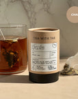 Tea canister labeled 'Tea with Tae' next to a glass of tea on a marble surface.