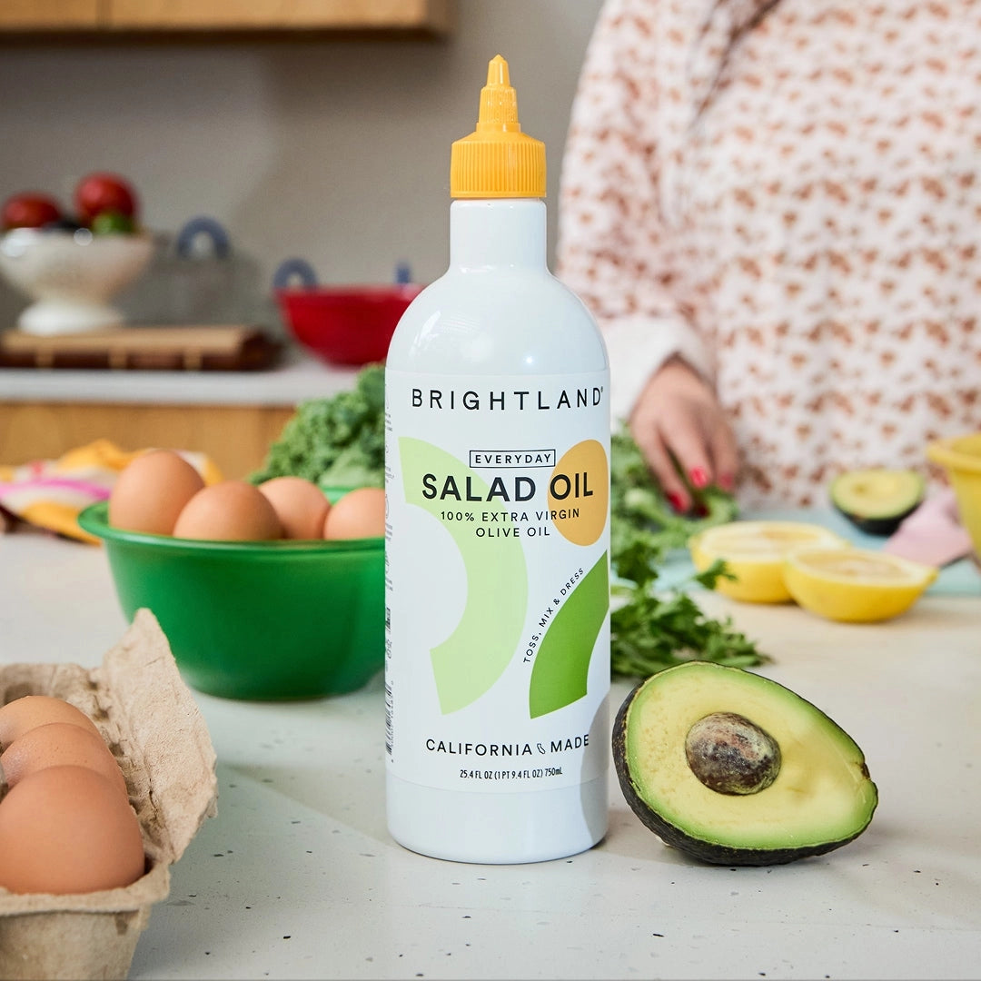 Bottle of Brightland salad oil on a kitchen counter with avocados and eggs.