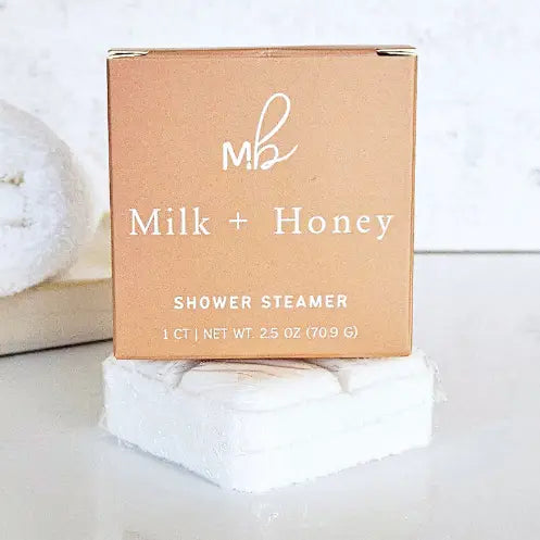 orange shower steamer packaging on top of a white shower steamer with white writing that says milk and honey