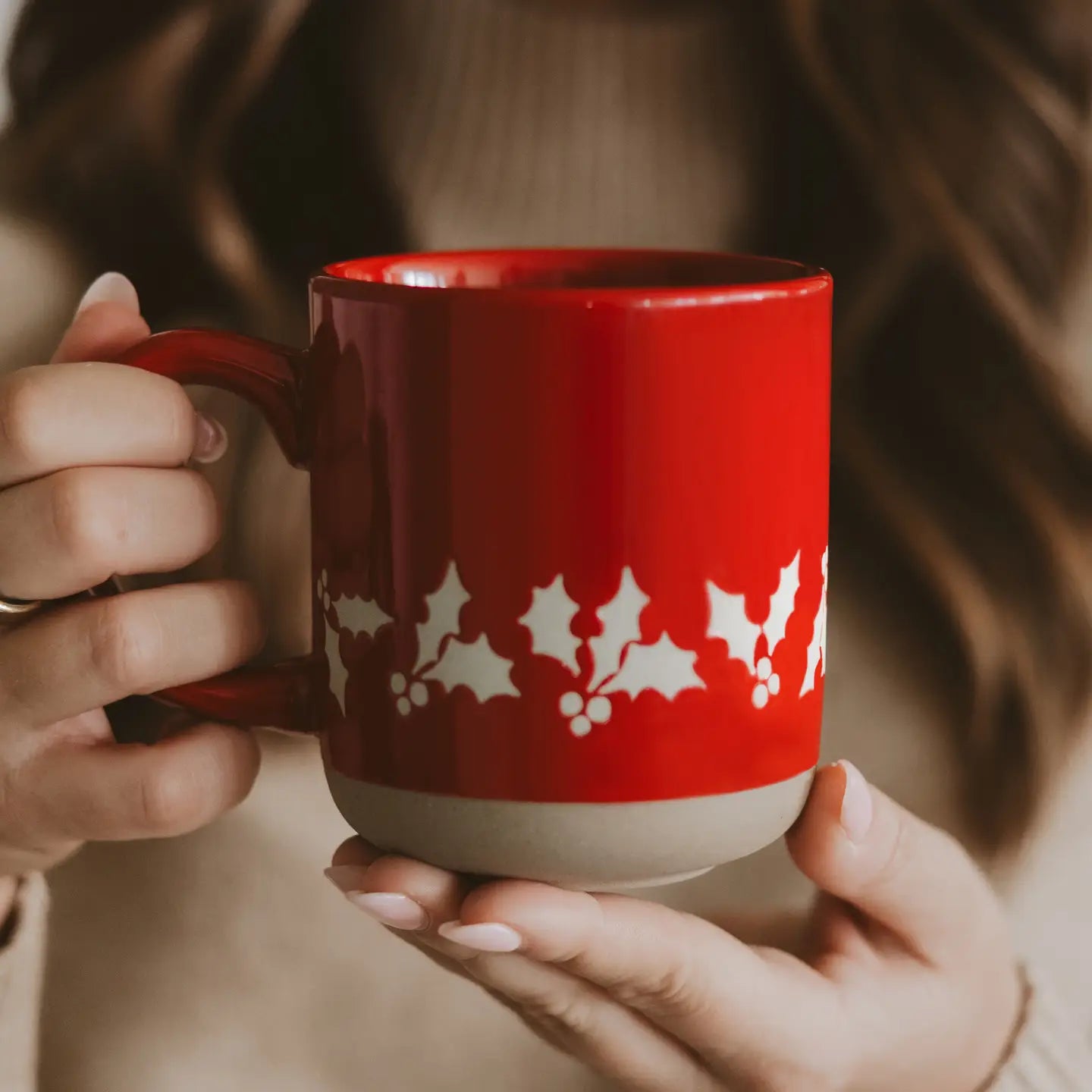 Red mug with white holly design held by a person