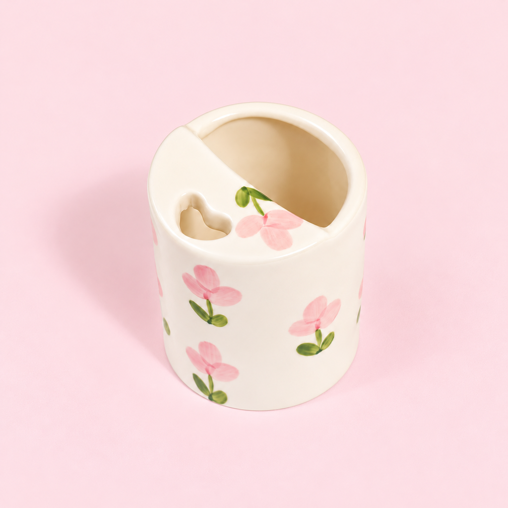 A white ceramic tooth holder with a pink floral pattern, featuring a heart-shaped cutout on the side, set against a solid light pink background.