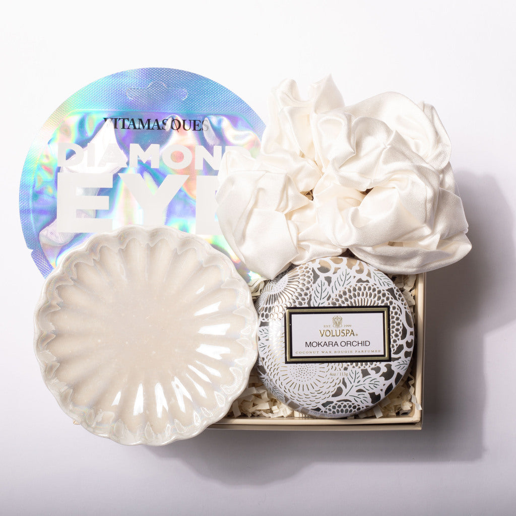 A luxury eye makeup remover gift set in a wooden box, featuring a round iridescent lid with 'ITAMA QUE DIAMOND EYE' text, a white ceramic brush, a white silk eye mask, and a round packaged product labeled 'VOLUSPA MOKARA ORCHID'.