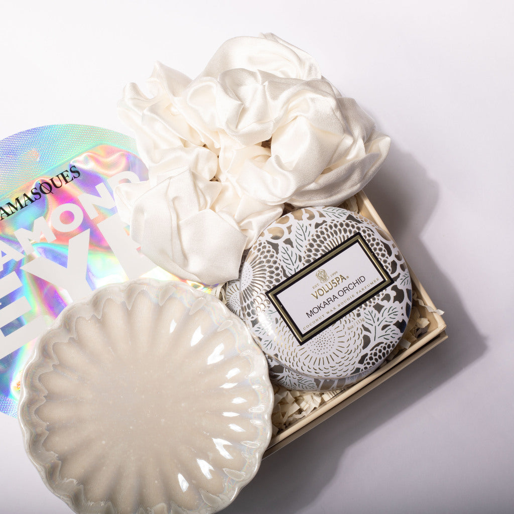 A curated gift set in a light wood box featuring a round L'OUSEA Moroccan Ground soap tin with a white lace pattern, a large ivory satin scrunchie, a matching scalloped ivory dish, and a holographic iridescent pouch. The L'OUSEA brand label is clearly visible on the soap tin.