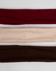 three headbands in different colors. The headbands are arranged in a vertical stack, with a burgundy headband on top, a beige or cream-colored headband in the middle, and a dark brown headband at the bottom. 